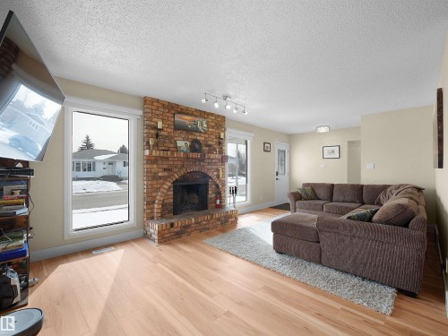 Living area featuring wood-finish flooring, a brick fireplace with an arched opening, and two large windows - 11044 166 Avenue, Edmonton, AB - Indoor Photo Showing Living Room With Fireplace