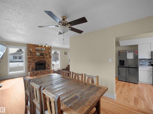 Open-concept living space featuring a brick fireplace with an arched firebox, light wood-finish flooring, and a ceiling fan with integrated lighting - 11044 166 Avenue, Edmonton, AB - Indoor Photo Showing Dining Room With Fireplace