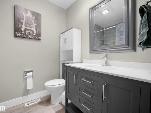 Bathroom featuring a dark gray vanity with chrome hardware, a white countertop with an integrated sink, a framed mirror, and wood-finish flooring - 11044 166 Avenue, Edmonton, AB - Indoor Photo Showing Bathroom