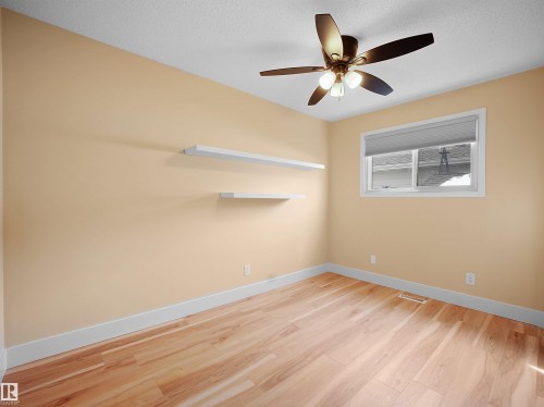 Room featuring wood-finish flooring, a ceiling fan with integrated lighting, a window with a roller shade, and two wall-mounted floating shelves - 11044 166 Avenue, Edmonton, AB - Indoor Photo Showing Other Room