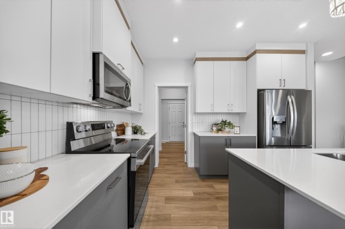 Modern kitchen featuring two-tone cabinetry, stainless steel appliances, white countertops, and wood-finish flooring - 20723 24 Avenue, Edmonton, AB - Indoor Photo Showing Kitchen With Upgraded Kitchen