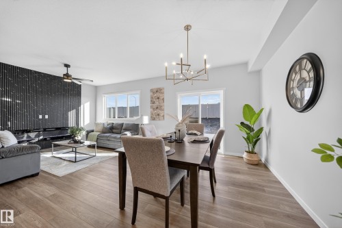 Open-concept living and dining area featuring wood-finish flooring, a contemporary chandelier, recessed lighting, and a unique black textured accent wall - 20723 24 Avenue, Edmonton, AB - Indoor