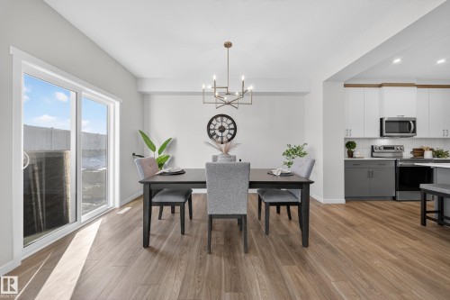 Open-concept dining area featuring wood-finish flooring, a contemporary chandelier, and a sliding glass door - 20723 24 Avenue, Edmonton, AB - Indoor