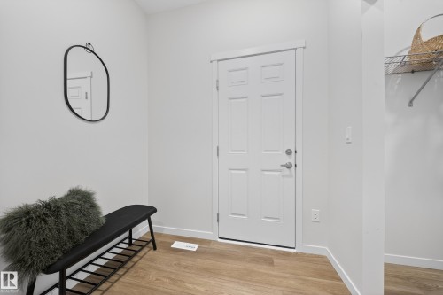 Bright entryway featuring a paneled door with brushed nickel hardware, wood-finish flooring, and crisp white walls - 20723 24 Avenue, Edmonton, AB - Indoor Photo Showing Other Room