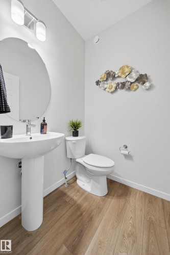 Pedestal sink with chrome faucet, complemented by a large circular mirror and modern vanity lighting - 20723 24 Avenue, Edmonton, AB - Indoor Photo Showing Bathroom