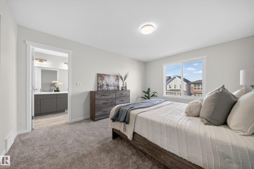 Carpeted bedroom featuring a clear window, flush-mount ceiling light, and access to a bathroom with a double vanity and wall-mounted light fixtures - 20723 24 Avenue, Edmonton, AB - Indoor Photo Showing Bedroom