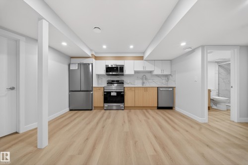 Modern kitchen featuring stainless steel appliances, light wood-finish flooring, two-tone cabinetry, and a marble-look backsplash - 20723 24 Avenue, Edmonton, AB - Indoor Photo Showing Kitchen