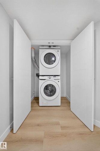 Dedicated laundry closet featuring a stacked white washer and dryer, light wood-finish flooring, and white bifold doors - 20723 24 Avenue, Edmonton, AB - Indoor Photo Showing Laundry Room