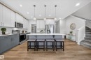 Open-concept kitchen with a large island featuring pendant lighting, two-tone cabinetry, stainless steel appliances, and wood-finish flooring - 20723 24 Avenue, Edmonton, AB  - Indoor Photo Showing Kitchen With Upgraded Kitchen 