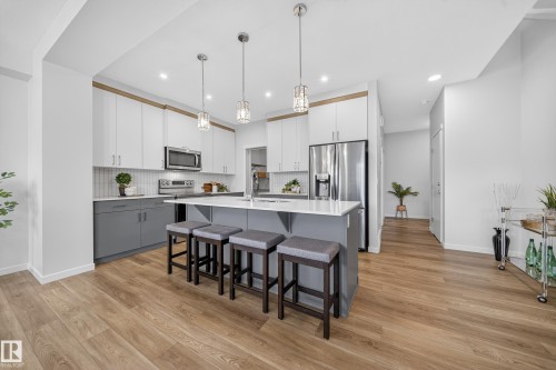 Open-concept kitchen featuring an island with counter seating, stainless steel appliances, pendant lighting, wood-finish flooring, and two-tone cabinetry - 20723 24 Avenue, Edmonton, AB - Indoor Photo Showing Kitchen With Upgraded Kitchen