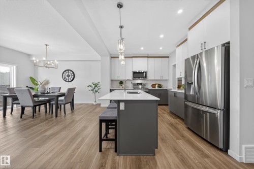 Open-concept kitchen and dining area featuring wood-finish flooring, a kitchen island with seating, stainless steel appliances, and contemporary pendant lighting - 20723 24 Avenue, Edmonton, AB - Indoor