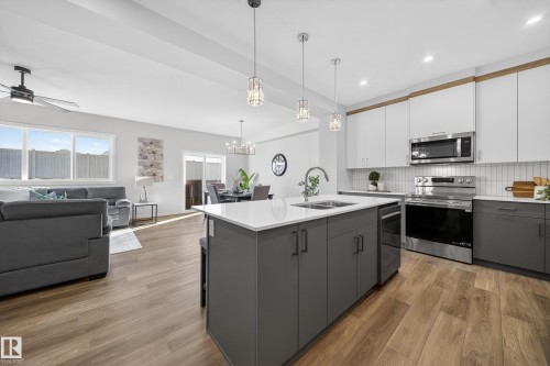 Open-concept living area featuring a modern kitchen island with pendant lighting, stainless steel appliances, wood-finish flooring, and expansive windows - 20723 24 Avenue, Edmonton, AB - Indoor Photo Showing Kitchen With Double Sink With Upgraded Kitchen