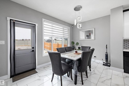 Dining area with white-toned flooring, modern pendant lighting, and a large window with horizontal blinds - 714 Ebbers Place, Edmonton, AB - Indoor Photo Showing Dining Room