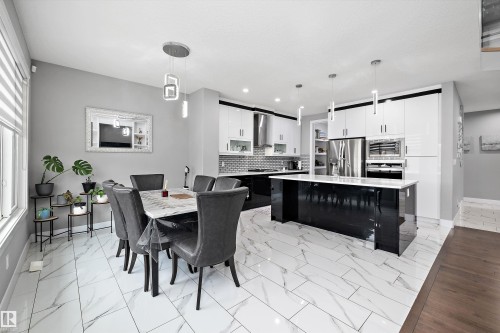 Open-concept kitchen and dining area featuring large format tile flooring, a central kitchen island with a light-toned countertop, glossy white upper cabinetry, and stainless steel appliances - 714 Ebbers Place, Edmonton, AB - Indoor Photo Showing Dining Room