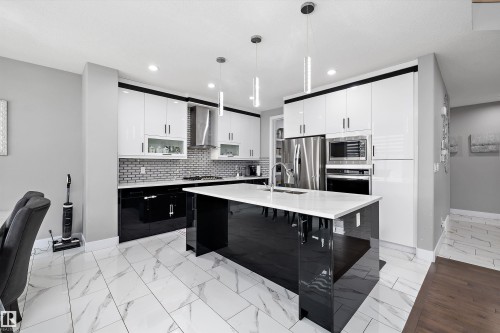Modern kitchen featuring a large central island with a solid surface countertop, white and black high-gloss cabinetry, stainless steel appliances, and a tiled backsplash - 714 Ebbers Place, Edmonton, AB - Indoor Photo Showing Kitchen With Upgraded Kitchen