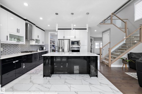 Gourmet kitchen featuring a large island with pendant lighting, white countertops, black and white cabinetry, stainless steel appliances, and a subway tile backsplash - 714 Ebbers Place, Edmonton, AB - Indoor Photo Showing Kitchen With Upgraded Kitchen