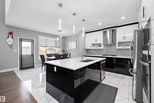 Open-concept kitchen featuring a large island with white countertop, black high-gloss cabinetry, and pendant lighting - 714 Ebbers Place, Edmonton, AB - Indoor Photo Showing Kitchen With Stainless Steel Kitchen With Upgraded Kitchen