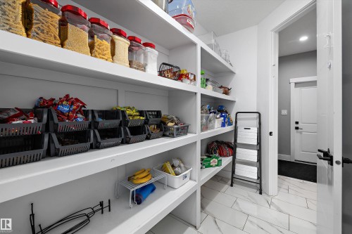 Walk-in pantry featuring built-in shelving, white tile flooring, and a solid core door with contemporary hardware - 714 Ebbers Place, Edmonton, AB - Indoor With Storage