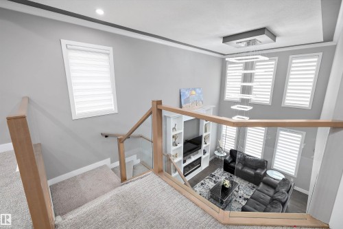 Open-concept living space featuring a two-story ceiling, a contemporary fireplace with built-in shelving, and a modern chandelier - 714 Ebbers Place, Edmonton, AB - Indoor Photo Showing Other Room