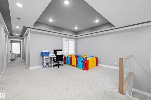 Spacious carpeted room featuring a double tray ceiling with recessed lighting, a window with horizontal blinds, and a glass panel railing - 714 Ebbers Place, Edmonton, AB - Indoor Photo Showing Other Room