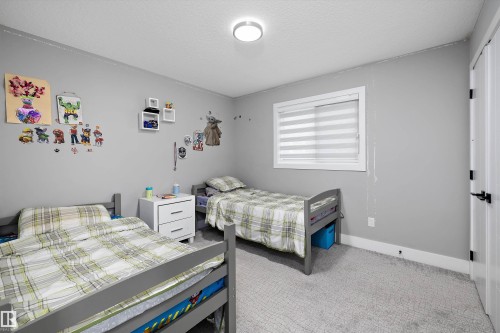 Bedroom featuring light gray walls, textured carpet flooring, a white trim window with blinds, and a white interior door with matte black hardware - 714 Ebbers Place, Edmonton, AB - Indoor Photo Showing Bedroom