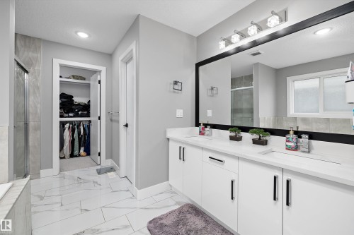 Spacious bathroom featuring a dual vanity with white cabinetry and countertops, a large framed mirror, recessed lighting, and a walk-in shower with tiled walls - 714 Ebbers Place, Edmonton, AB - Indoor Photo Showing Bathroom