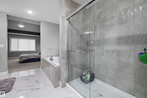 Glass-enclosed shower with gray tiled walls and a built-in shelf, alongside a white drop-in bathtub with matching gray tile surround - 714 Ebbers Place, Edmonton, AB - Indoor Photo Showing Bathroom