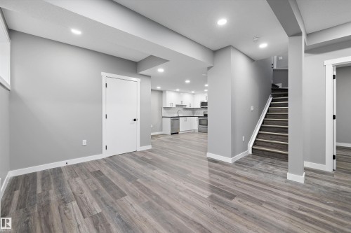 Spacious lower level featuring wood-finish flooring, recessed lighting, and a modern kitchen with white cabinetry - 714 Ebbers Place, Edmonton, AB - Indoor Photo Showing Other Room