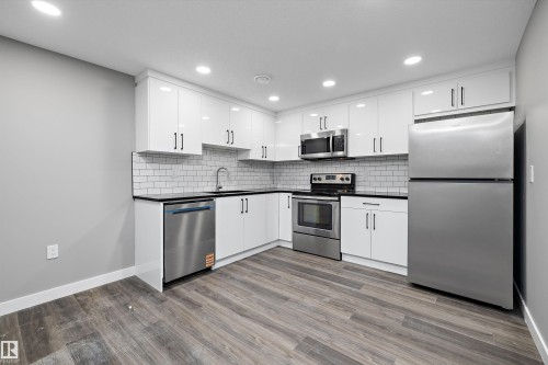 Modern kitchen featuring white shaker cabinetry, black countertops, stainless steel appliances, a subway tile backsplash, and wood-finish flooring - 714 Ebbers Place, Edmonton, AB - Indoor Photo Showing Kitchen With Stainless Steel Kitchen With Upgraded Kitchen