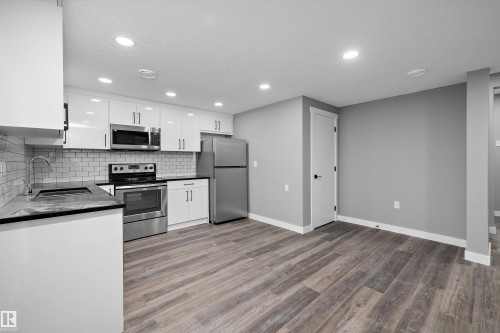 Kitchen area featuring glossy white cabinetry with dark hardware, stainless steel appliances, a subway tile backsplash, dark countertops, and wood-finish flooring - 714 Ebbers Place, Edmonton, AB - Indoor Photo Showing Kitchen With Stainless Steel Kitchen