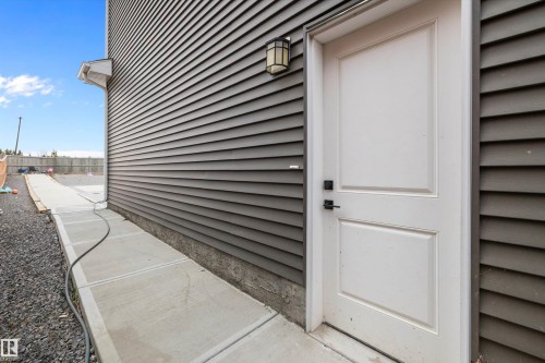 White panel door with black hardware, complementing the dark gray horizontal siding and concrete pathway - 714 Ebbers Place, Edmonton, AB - Outdoor With Exterior