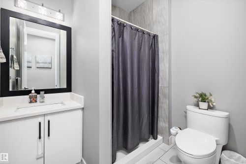 Contemporary bathroom featuring a white vanity with a quartz countertop and integrated sink, a black framed mirror, and a full shower with textured wall tile and a white base - 714 Ebbers Place, Edmonton, AB - Indoor Photo Showing Bathroom