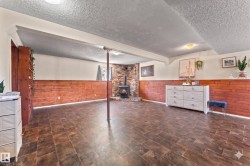 Spacious room featuring wood-finish flooring, wood-paneled wainscoting, and a brick fireplace with a wood-burning stove - 