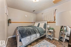 Bedroom with wood-finish tile flooring, neutral-toned walls, a partial window with privacy curtains, and white trim molding - 