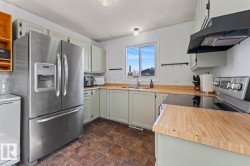 Kitchen featuring light green cabinetry with brushed nickel hardware, wood-finish countertops, and a stainless steel French-door refrigerator - 