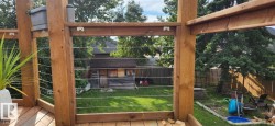 Wood-finish deck with cable railing overlooking a fenced backyard featuring a storage shed and mature trees - 