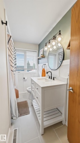 White vanity with a light countertop, black fixtures, and a circular mirror - 23 Clearwater, Devon, AB - Indoor Photo Showing Bathroom