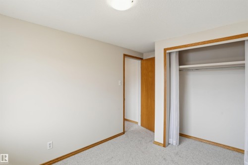 Carpeted room featuring a built-in closet with sliding doors, a wood-finish door, light-toned walls, and wood-trim baseboards - 23 Clearwater, Devon, AB - Indoor Photo Showing Other Room