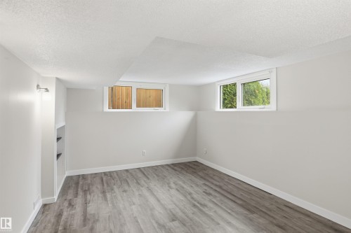 Spacious room featuring wood-finish flooring, light grey walls, white trim, and two egress windows - 23 Clearwater, Devon, AB - Indoor Photo Showing Other Room