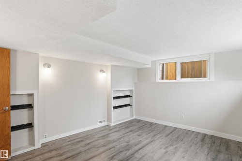 Spacious finished room featuring wood-finish flooring, recessed built-in shelving, sconce lighting, and a white-framed window - 23 Clearwater, Devon, AB - Indoor Photo Showing Other Room