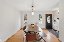 Spacious room featuring wood-finish flooring, white walls, and a black front door with an oval decorative glass insert - 