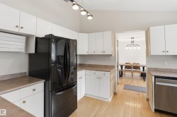 Kitchen featuring light wood-finish flooring, white cabinetry with gold-tone hardware, a black refrigerator, and light-toned countertops - 