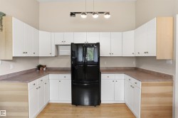U-shaped kitchen featuring white cabinetry, light wood-finish flooring, and a black refrigerator - 