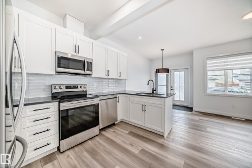 Modern kitchen featuring white shaker cabinetry, stainless steel appliances, dark countertops, and a full tile backsplash - 38 1910 Collip View, Edmonton, AB - Indoor Photo Showing Kitchen With Upgraded Kitchen