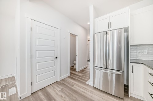Modern kitchen area featuring a stainless steel French door refrigerator, white shaker cabinetry, and wood-finish flooring - 38 1910 Collip View, Edmonton, AB - Indoor Photo Showing Kitchen