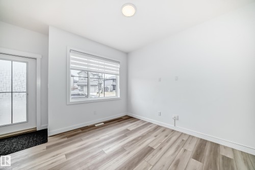Bright room featuring wood-finish flooring, white walls, and a large window with horizontal blinds - 38 1910 Collip View, Edmonton, AB - Indoor Photo Showing Other Room