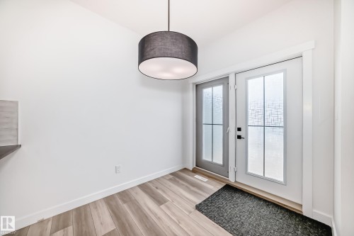 Double French doors with frosted glass panels, wood-finish flooring, and a modern drum pendant light - 38 1910 Collip View, Edmonton, AB - Indoor Photo Showing Other Room