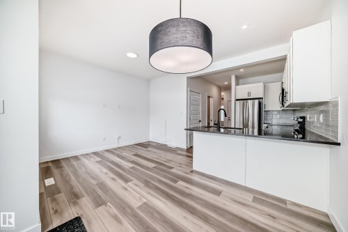 Open-concept living area featuring wood-finish flooring, a modern drum pendant light, and a kitchen bar with a dark countertop - 38 1910 Collip View, Edmonton, AB - Indoor Photo Showing Kitchen