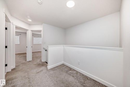Carpeted landing area featuring a white railing, contemporary doors with black hardware, recessed lighting, and crisp white walls - 38 1910 Collip View, Edmonton, AB - Indoor Photo Showing Other Room