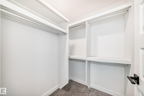White built-in closet system with multiple shelving units and hanging rods, complemented by gray carpet flooring and a door with black hardware - 38 1910 Collip View, Edmonton, AB - Indoor